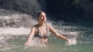 在热带丛林中飞溅的瀑布中享受淡水洗澡的快乐女人。 快乐的女人游泳